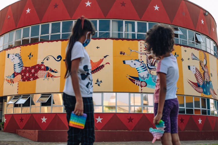 Girls Standing Near A Carnival With Mural