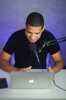 Man using laptop and microphone for podcast recording indoors. Engaging tech setup.