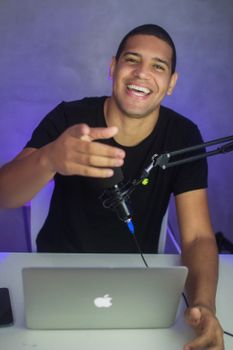 Cheerful male podcaster recording indoors with laptop and microphone. Perfect image for media or tech topics.