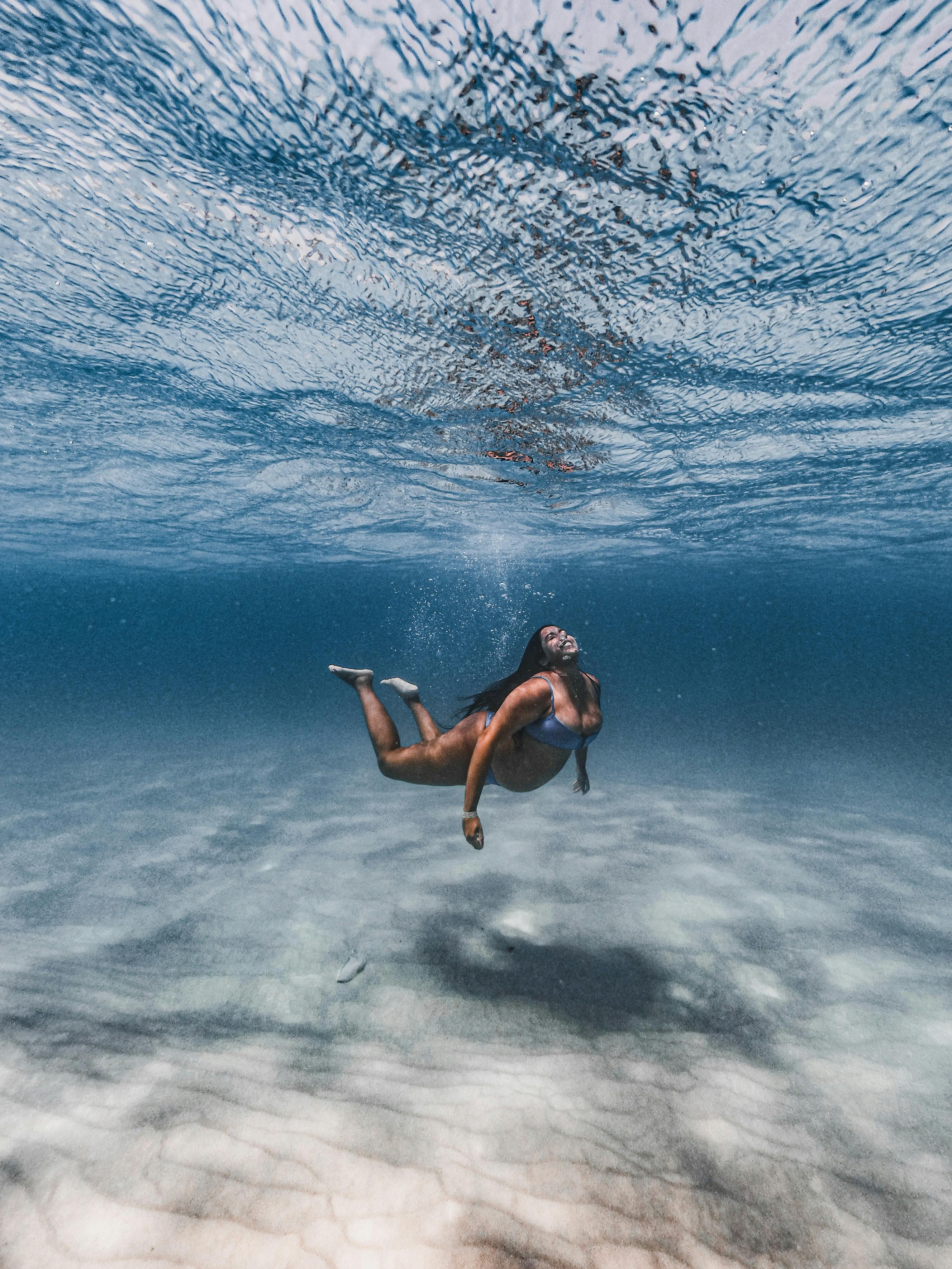 A Latina woman swimming gracefully underwater in a clear ocean, captured in daylight.