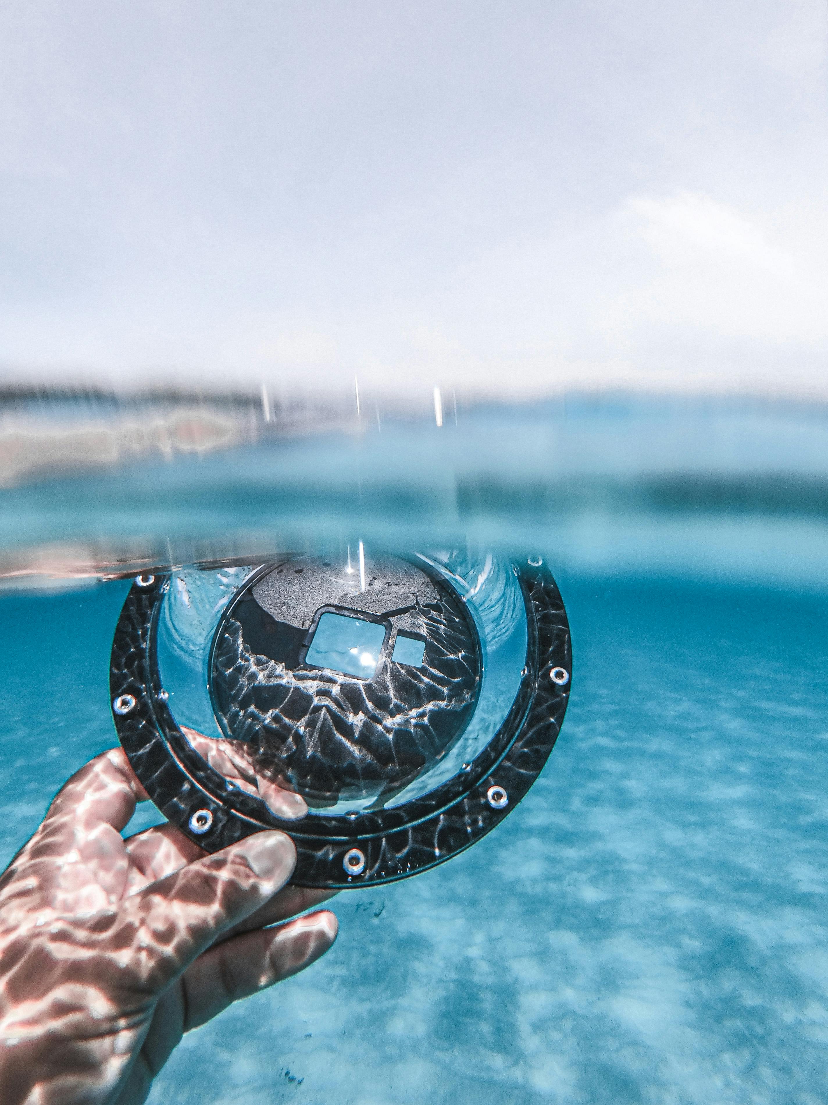 Hand holding dome port in clear water, creating artistic reflection.