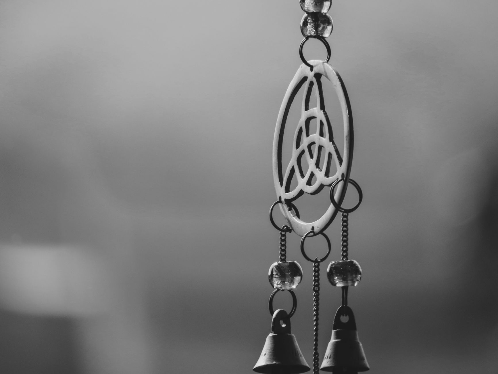 Artistic black and white close-up of a Celtic knot wind chime with bells.