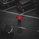 俯视视角下，一个人打着红伞在下雨的停车场行走