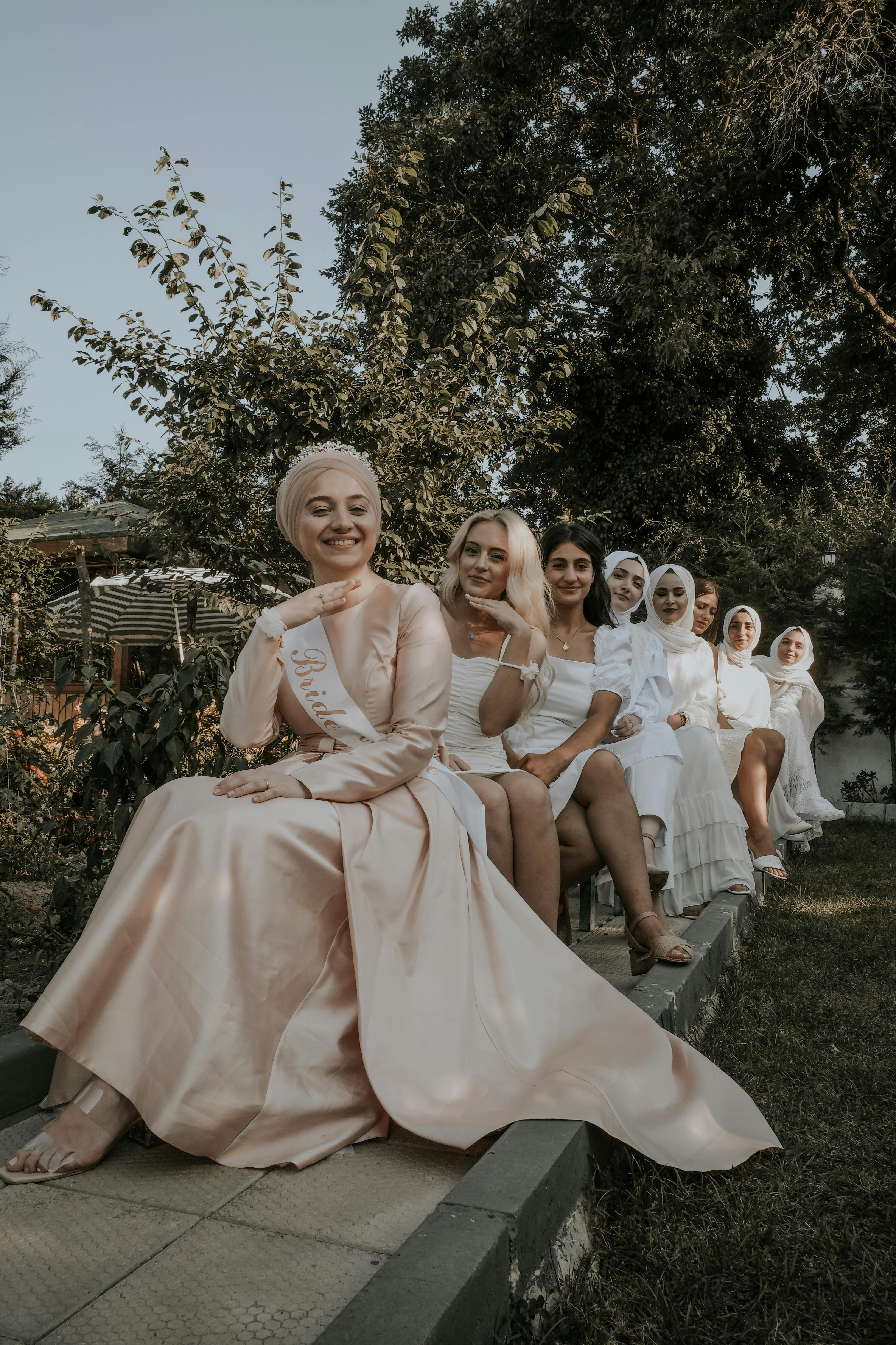 A group of women in hijabs and formal dresses posing joyfully outdoors, showcasing friendship.
