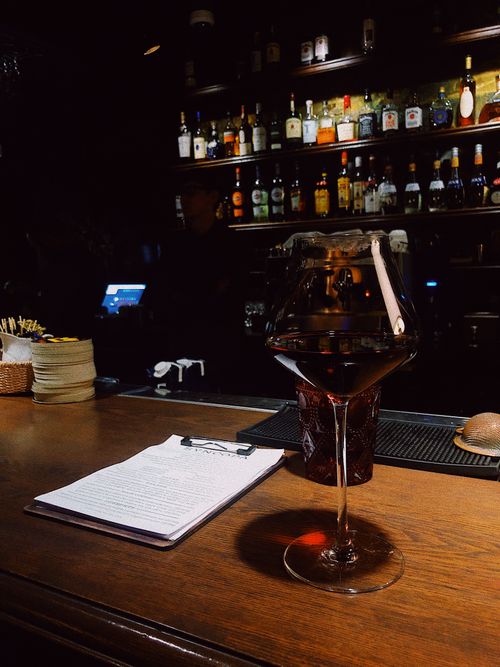 Free A dimly lit bar featuring a glass of red wine on the counter and shelves stocked with bottles. Stock Photo