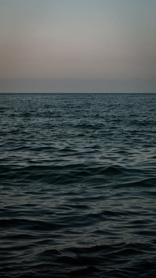Picturesque view of endless dark blue rippling seawater with horizon line under dark blue cloudy sky in evening