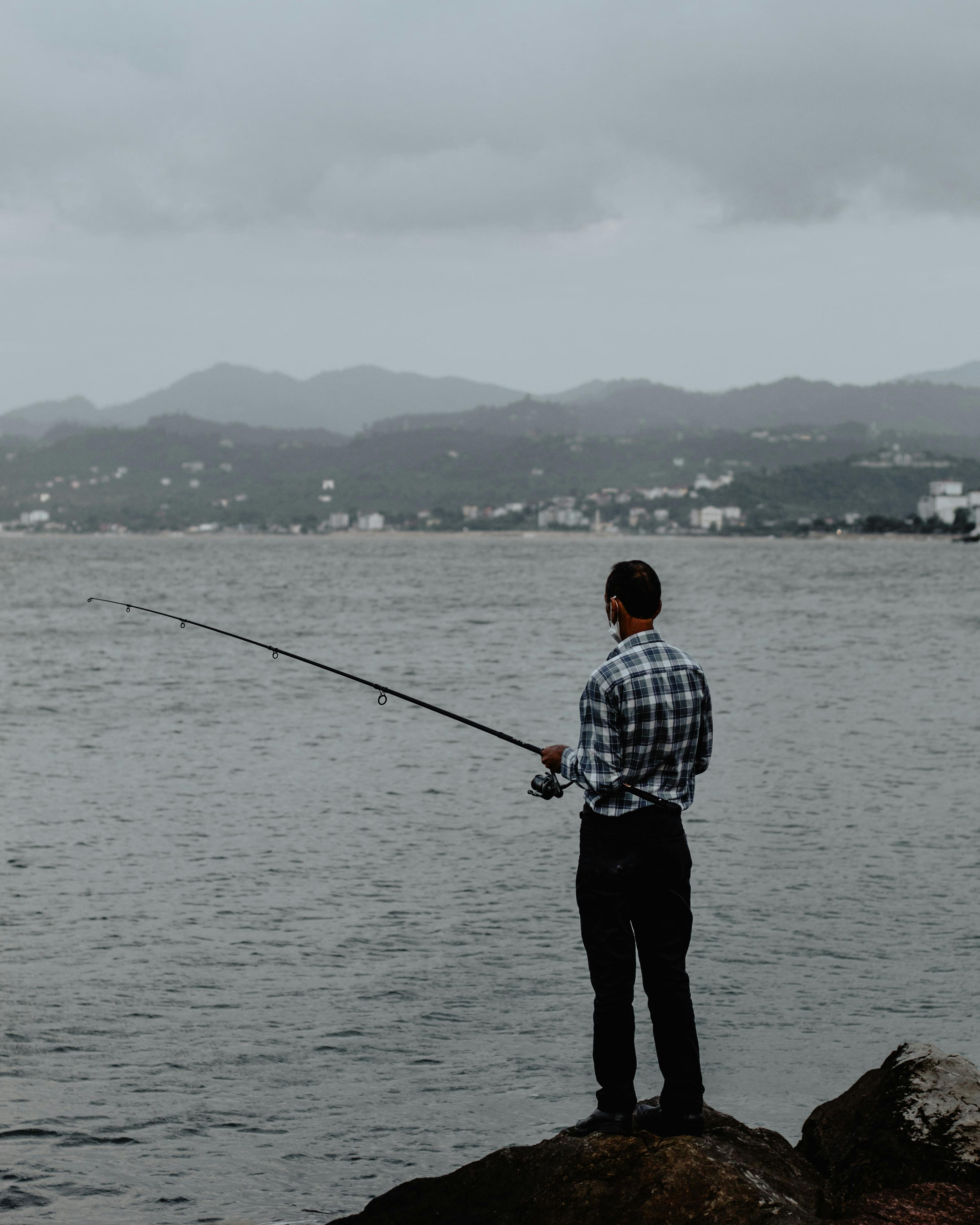 Download Man fishing at a serene lake with a high-quality fishing rod  Wallpaper