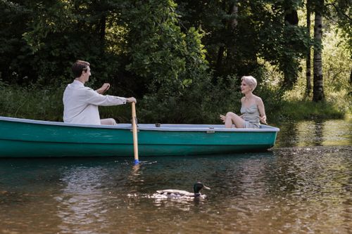 Free A couple enjoys a romantic boat ride on a tranquil lake, surrounded by lush greenery. Stock Photo