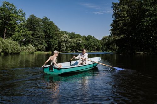 Free A couple rows a boat on a tranquil lake surrounded by lush greenery under a clear blue sky. Stock Photo
