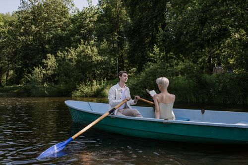 Free A serene boat ride on a lake with a man rowing and a woman reading. Stock Photo