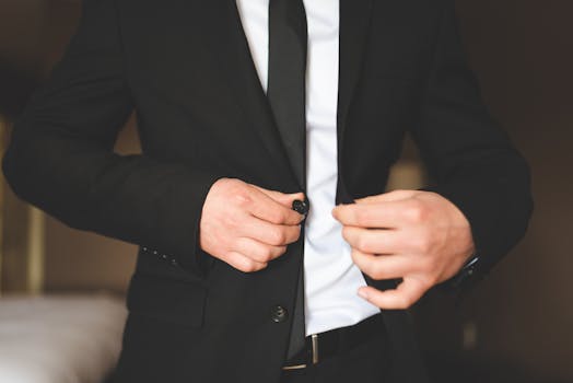 Close-up of a man in a black suit adjusting his jacket indoors.