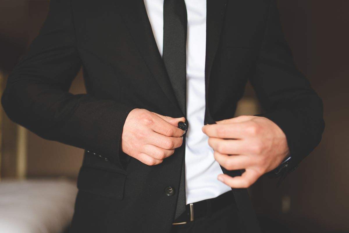 Close-up of a man fastening a tailored dark suit jacket.