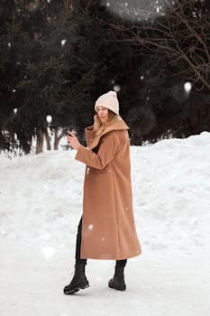 Woman in winter attire holding a cup, enjoying the snowy outdoors. Cozy and fashionable winter vibe.