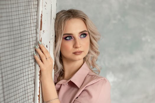 Beautiful woman with blonde hair and vibrant makeup posing indoors with a textured background.