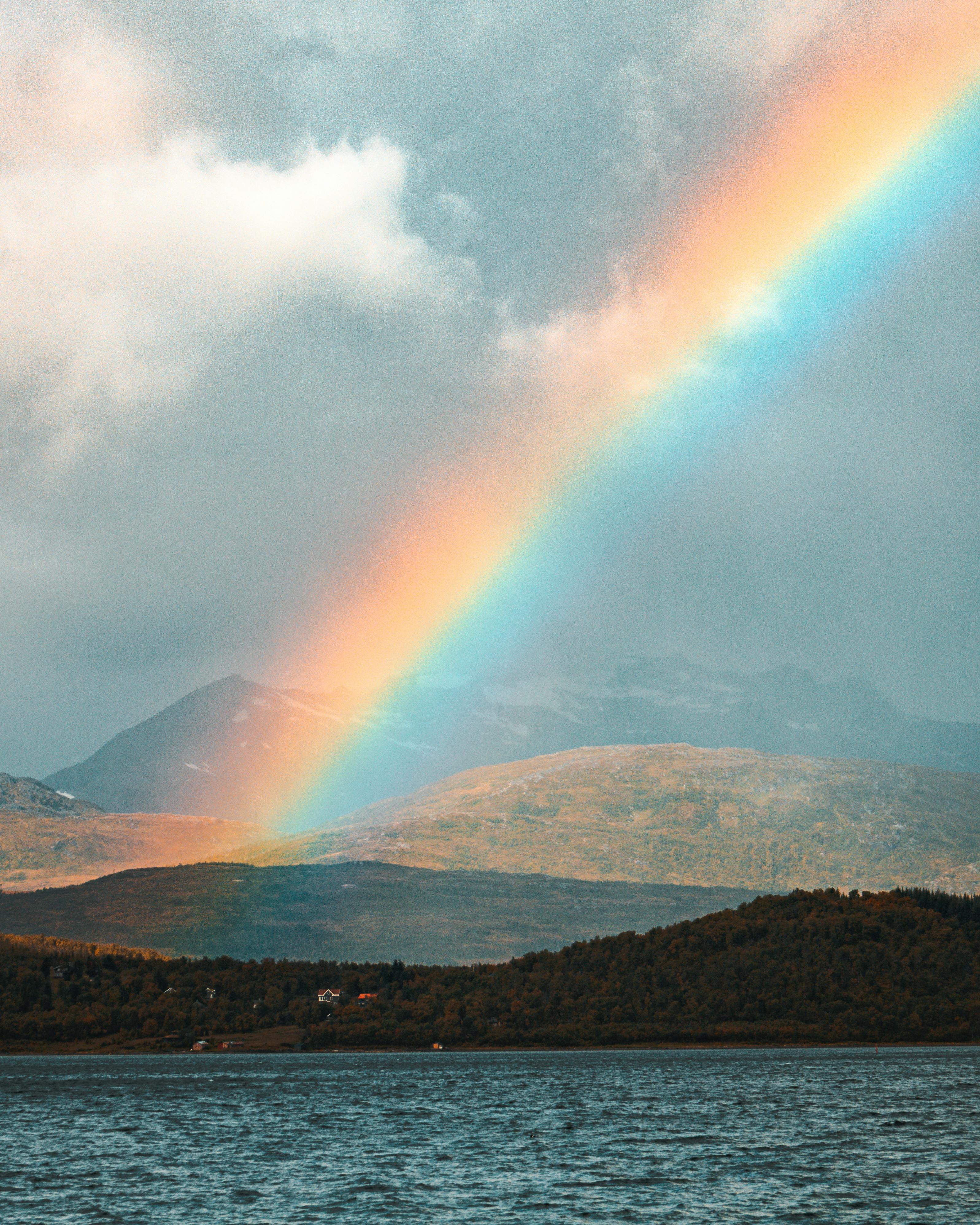 Vibrant rainbow arching over Tromsø's scenic fjord and mountains in Norway.