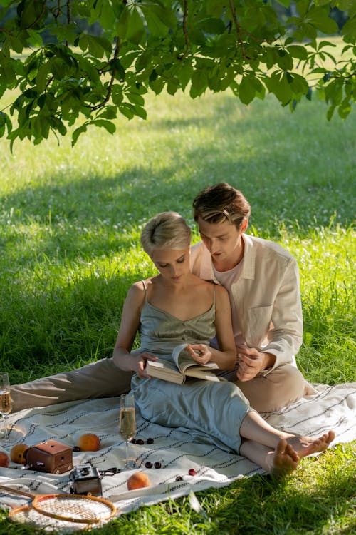 Couple Sitting on a Picnic Blanket While Reading a Book