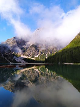 Tranquil view of Pragser Wildsee with misty mountains reflecting in the clear lake waters in Italy's Dolomites.