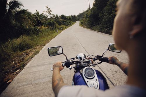 Free A tattooed biker rides through a serene, tree-lined road, enjoying the open air. Stock Photo