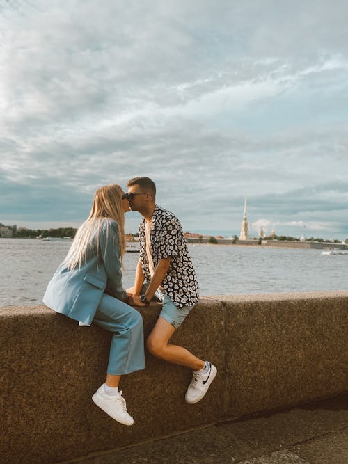 A Couple Kissing while Sitting on Concrete Wall Near Body of Water