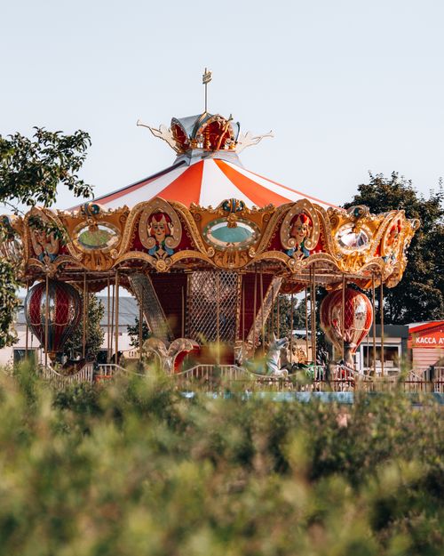 Free Vibrant carousel in an open fairground, surrounded by greenery, under a clear sky. Stock Photo