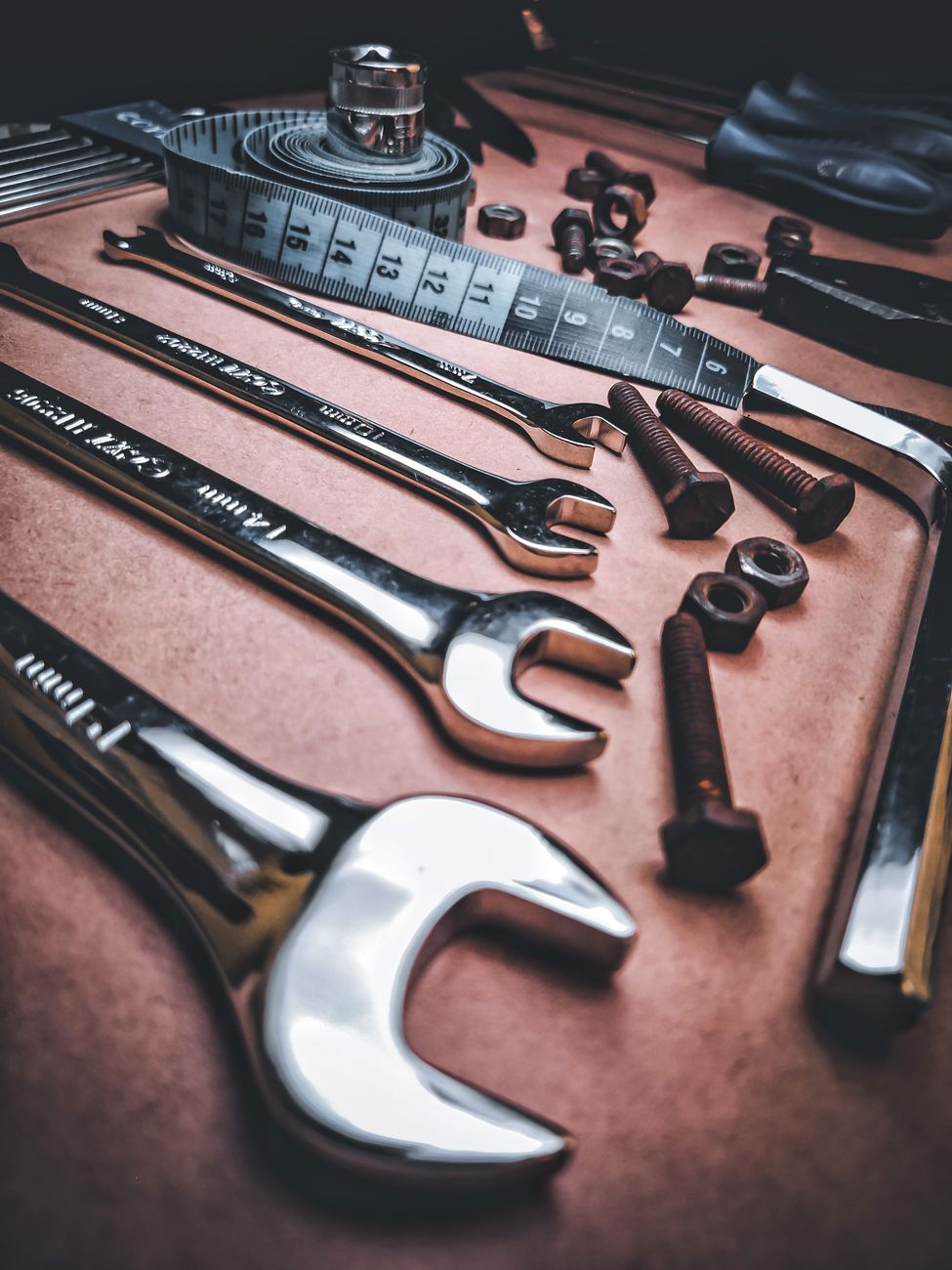Close-up view of various stainless steel tools, screws, and measuring tape on a workbench.