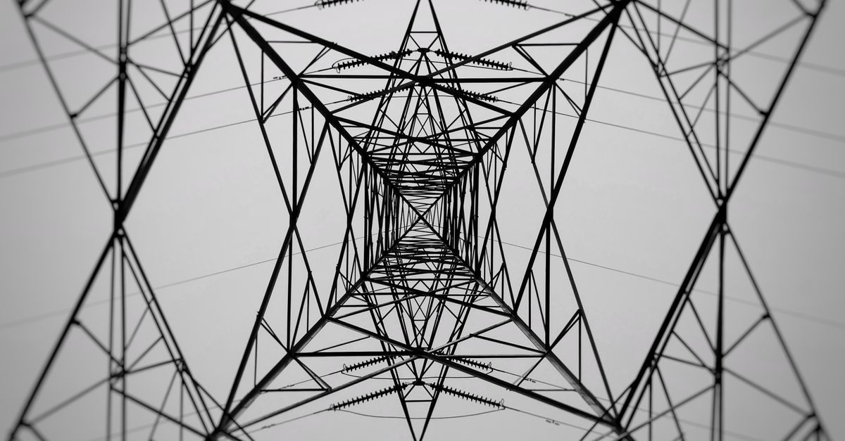 Monochrome low-angle shot of a power transmission tower in symmetrical perspective.