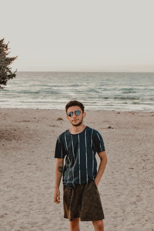 Photo of a Man in a Striped Shirt Standing at the Beach