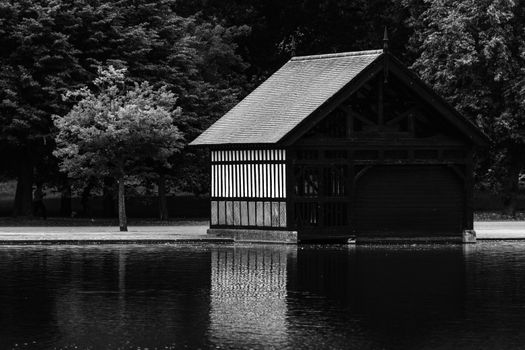 Black and white photo of a riverside cabin with reflections, set in England's serene landscape.