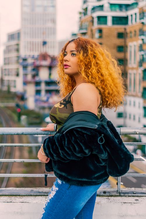 Free Fashionable woman with curly hair stands confidently in London, showcasing contemporary urban style. Stock Photo