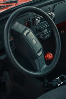 Close-up of vintage car interior showing steering wheel and red gearshift knob.