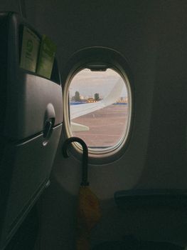 Looking out from an airplane window revealing an aircraft wing and yellow umbrella inside, ambient light.