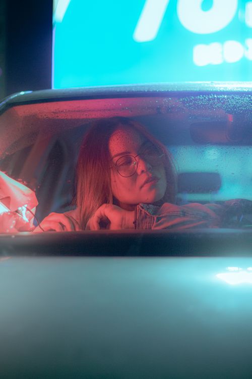 Free A woman with eyeglasses in a car at night, illuminated by neon lights. Stock Photo