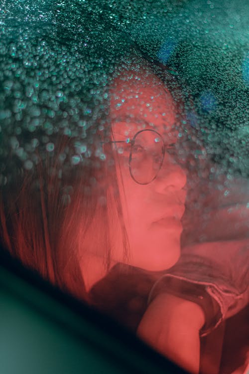 Free Portrait of a Woman Illuminated by a Red Light Behind Glass Stock Photo