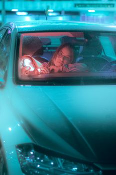 Moody night shot of a woman in a car with neon lighting creating a reflective atmosphere.