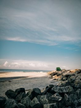 Peaceful beach scene with rocks, calming waves, and a bright sky.