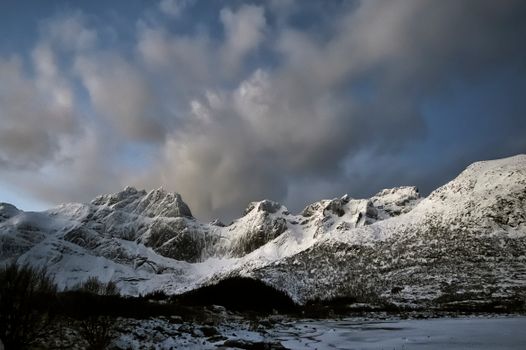A scenic view of snowcapped mountains under a dramatic sky in Nusfjord, Norway.