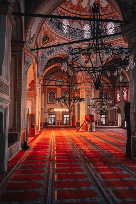 A beautifully ornate mosque interior showcasing chandeliers and vibrant red carpets under an intricately designed dome.