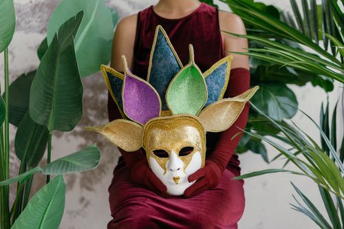 Free A woman in a velvet dress holding a colorful carnival mask amid lush houseplants, exuding elegance. Stock Photo