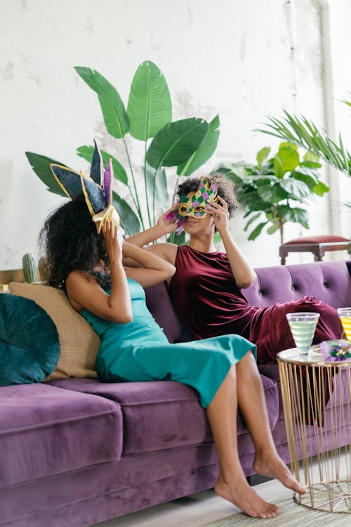 Women in Sleeveless Dresses Sitting on Purple Sofa