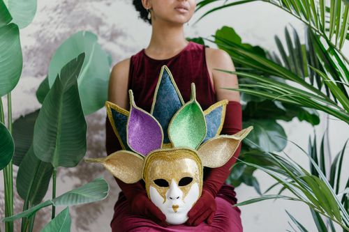 Free A woman holds a colorful Mardi Gras mask surrounded by tropical plants, evoking mystery and celebration. Stock Photo