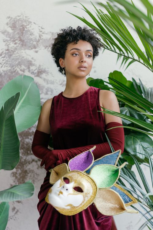 Free Stylish woman in velvet dress with a vibrant masquerade mask surrounded by lush greenery. Stock Photo