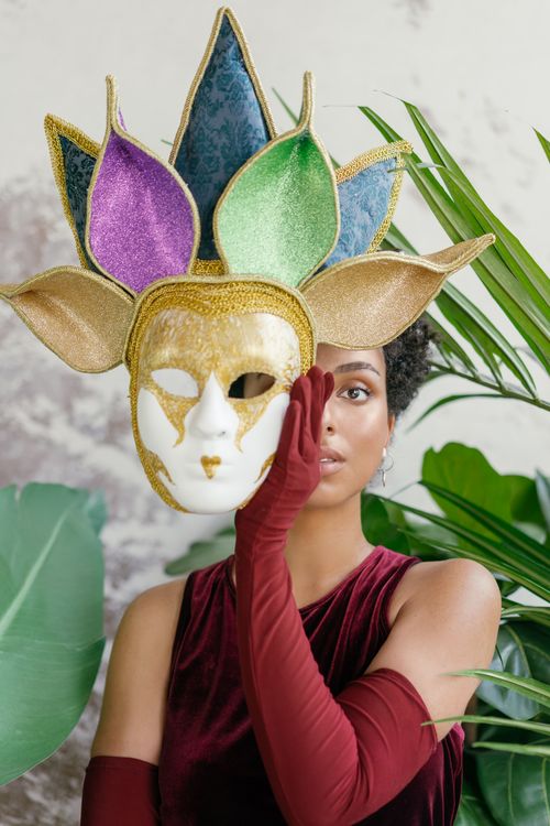 Free A woman in velvet attire holding an artistic carnival mask amidst lush greenery. Stock Photo