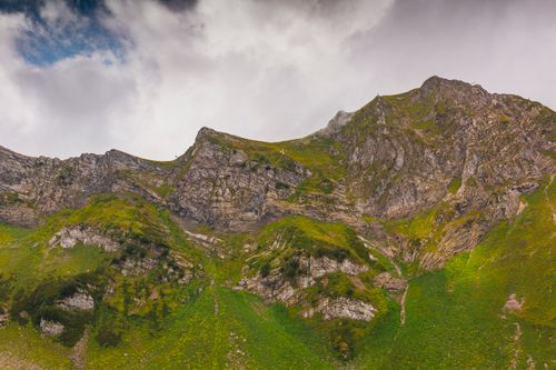 Free Stunning view of a lush green mountain landscape with a craggy cliff under a cloudy sky. Stock Photo