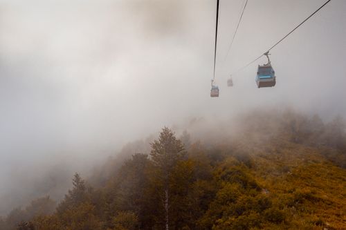 Free Cable cars moving through dense mist over autumnal mountains, creating a serene atmosphere. Stock Photo