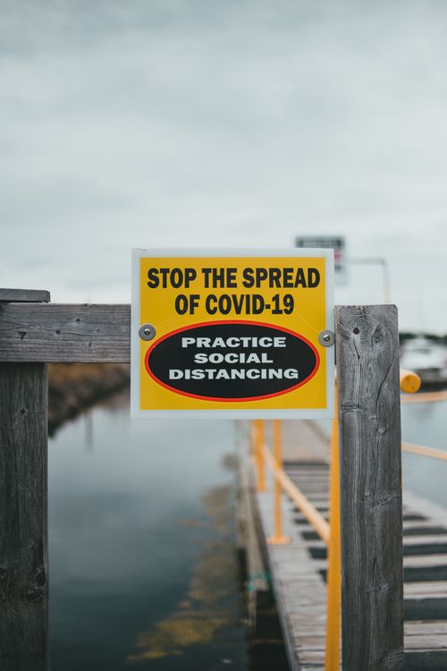 Free Yellow sign urging COVID-19 social distancing on a wooden dock. Stock Photo