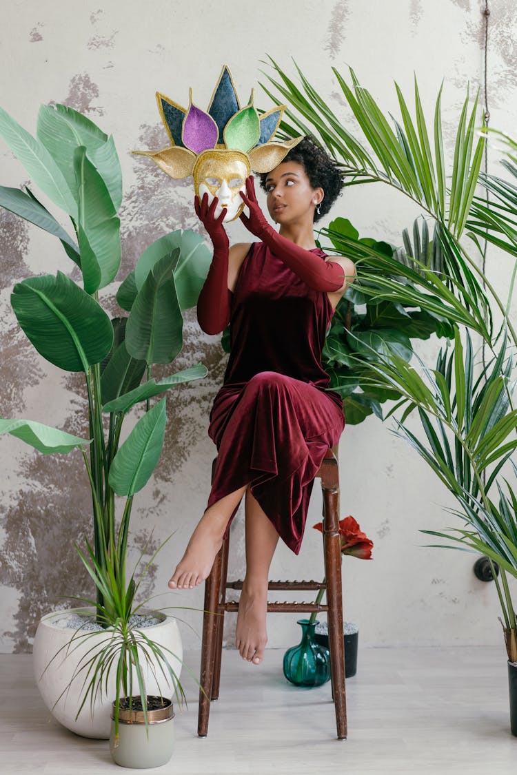 Woman Wearing A Maroon Velvet Dress Holding A Mask