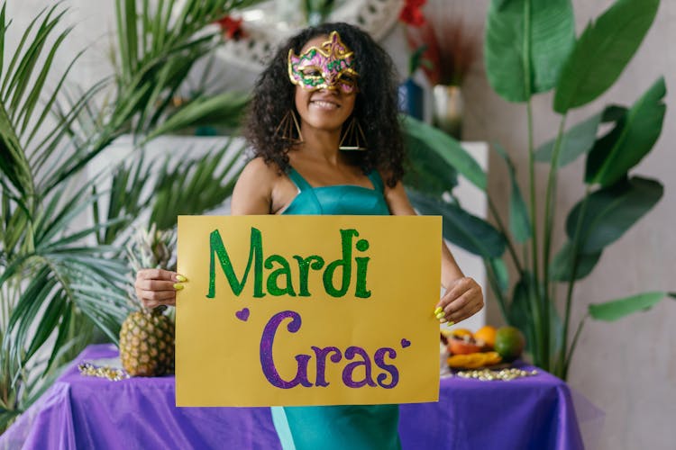 A Woman Wearing A Mask Holding A Mardi Gras Poster