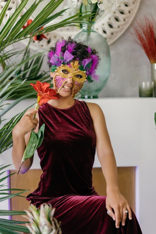 Woman in a Dress and Venetian Mask Sitting and Holding a Flower