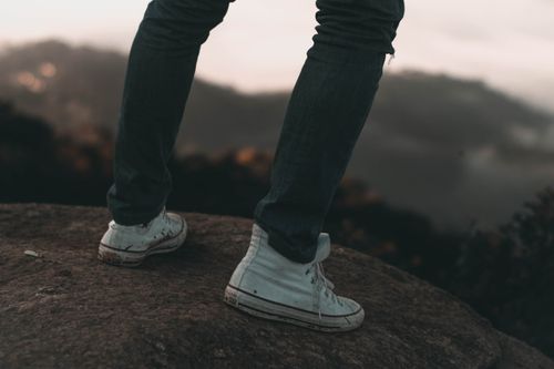 Free Close-up of person in denim jeans and sneakers standing on a rock, overlooking misty mountains. Stock Photo