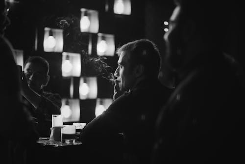 Grayscale Photo of a Man Smoking inside a Bar